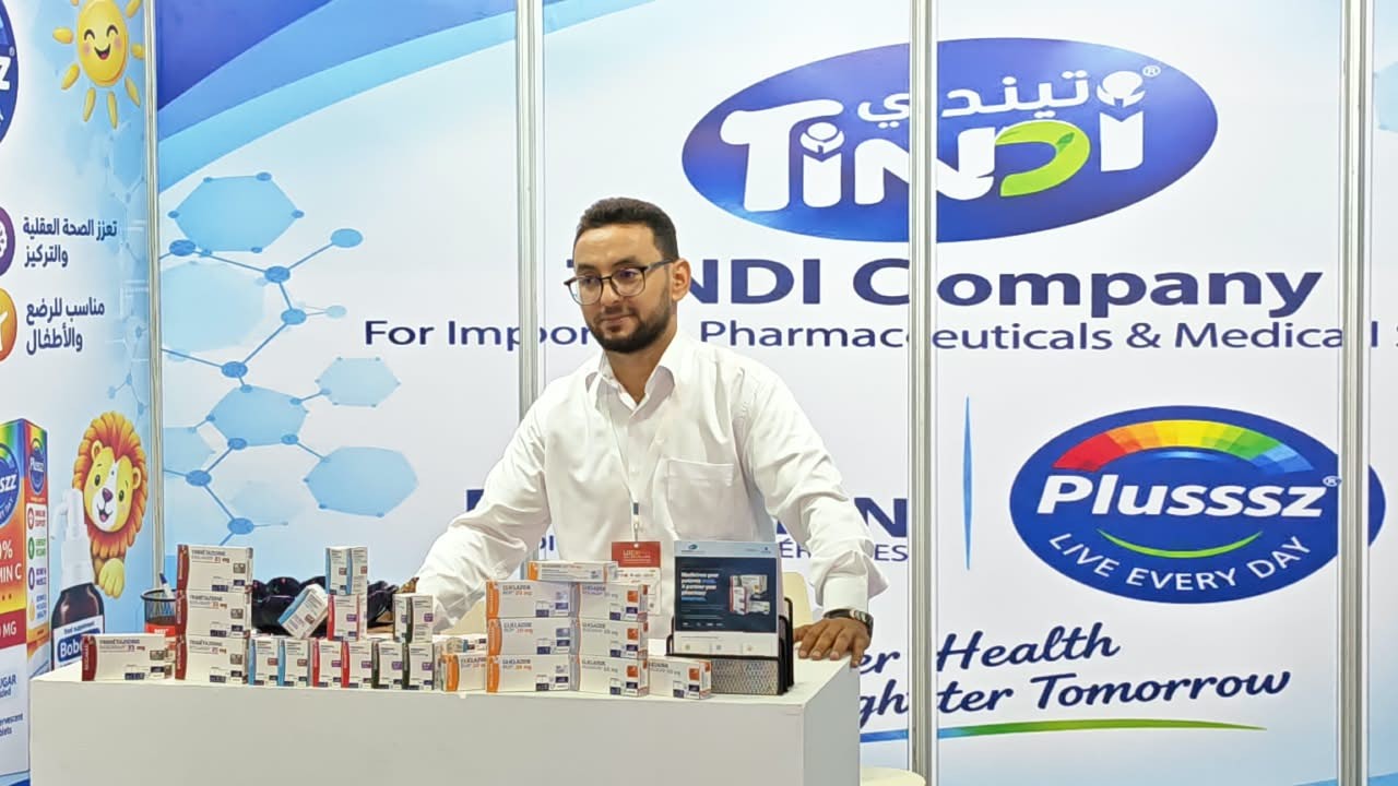 Un membre de l'équipe TINDI derrière le comptoir du stand, avec les marques Biogaran et Plusssz